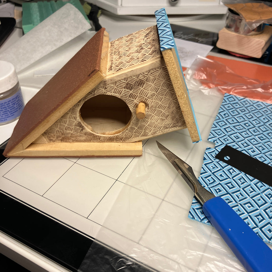 The birdhouse on it's side is being covered in different clay colors and patterns.