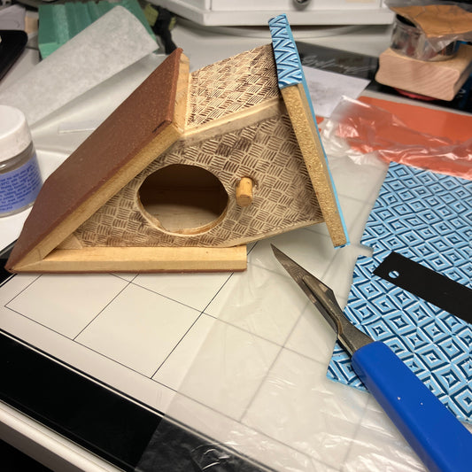 The birdhouse on it's side is being covered in different clay colors and patterns.