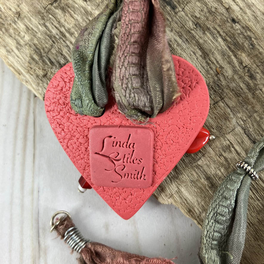 The red button heart pendant by Linda Stiles Smith is signed on the back with her signature stamp authenticating it as an LSS original necklace.