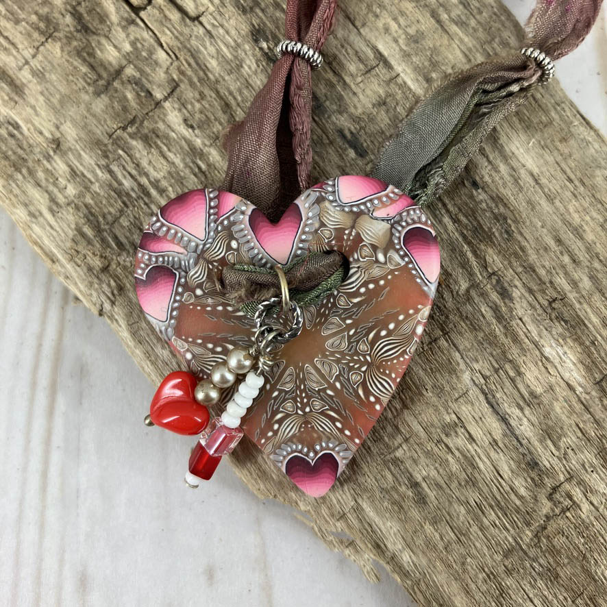 The focal piece of an original necklace design it is a heart covered in hearts with the dangle of a red heart bead and silver beads. Unique design by Linda Stiles Smith