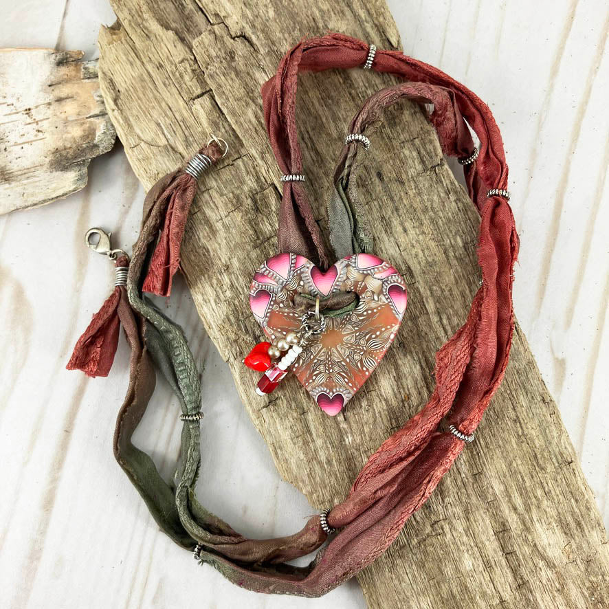 Full view of the button heart shaped necklace on a red and green sari silk full length of 30" with silver ring spacer beads. By Linda Stiles Smith of NatureScapes Studio.