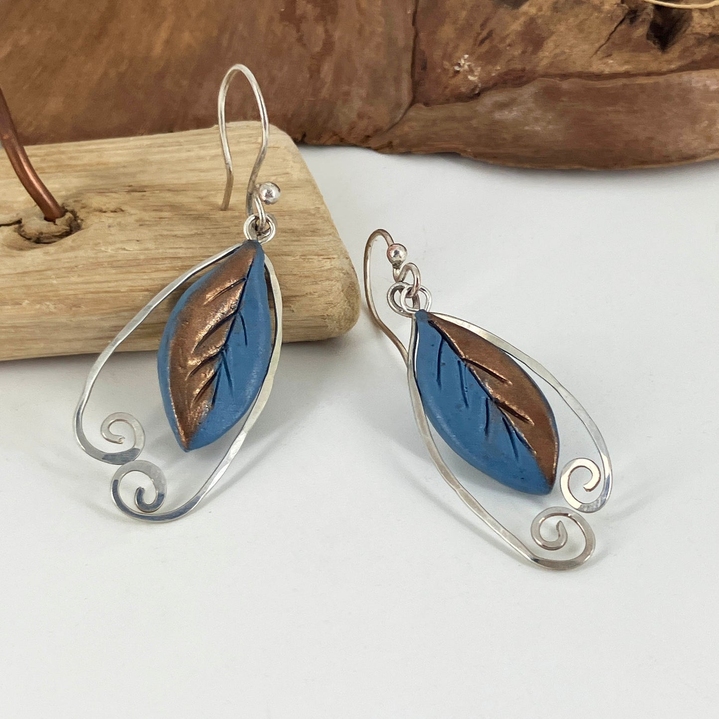 Leaf hook Earrings in blue and copper with sterling silver hooks and hammered wire swirls surround them. Designed by jewelry artist Linda Stiles Smith.