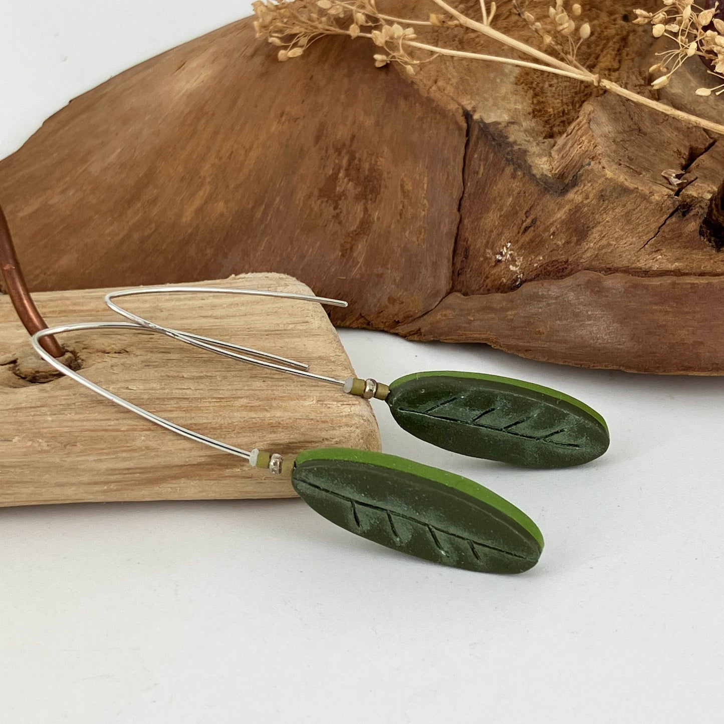 Layered colors of green on these oval leaf shaped earrings that drop from a long sterling silver hook. Handcrafted by Linda Stiles Smith