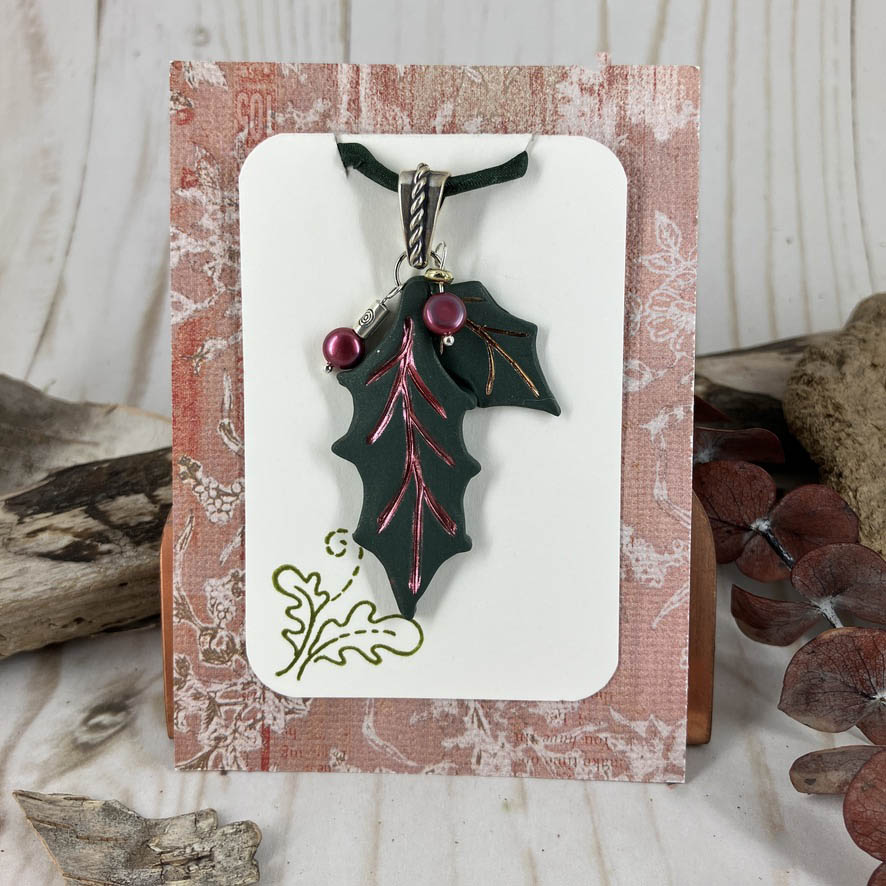 Gift card with green holly leaves with red and gold vein accents and cranberry pearl dangles on a sterling silver twist bail.