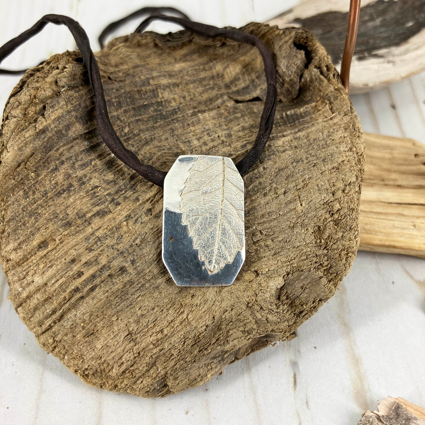 Bright fine silver pendant of real leaf imprinted into the metal surface of a necklace on black silk cording.