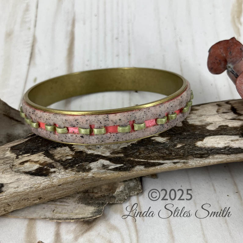 the appearance of stitches weaving in and out of a granite colored strip of clay is brought to life with shimmering coral and leaf green holes and strips. Design by Linda Stiles Smith of NatureScapes Studio.