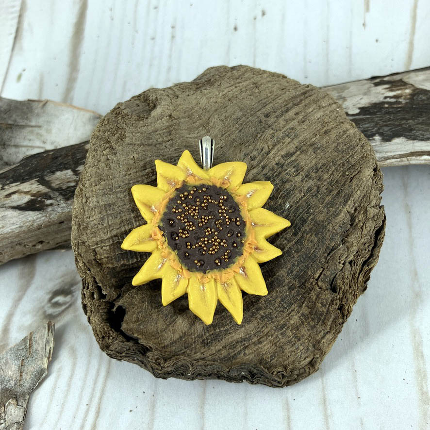 Close up of sunflower pendant in warm yellow colors with beaded center in brown and gold. Gift for flower lover women of all ages. Handcrafted by Linda Stiles Smith