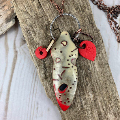 Hearts and dots patterns on the shiny smooth surface of the Symbol of Love pendant topped by red and ivory charms on a large metal ring. Handcrafted by Linda Stiles Smith