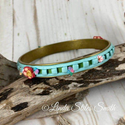 Layered blue and green bangle show tiny flowers popping from squares along the length of the bracelet. Artfully designed by Linda Stiles Smith.