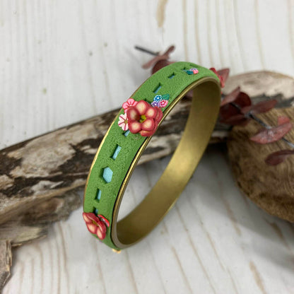 The kiss of spring flowers all around this Bangle bracelet are gather in bunches that seem to be growing out of the green grass. Built on a sturdy brass blank this creative use of clay and design is the brainchild of Linda Stiles Smith.