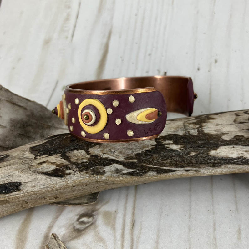 The ends of the open cuff shape are finished with a trio of the cuffs colors stacked into a flame shape finished with a metal bead tip.