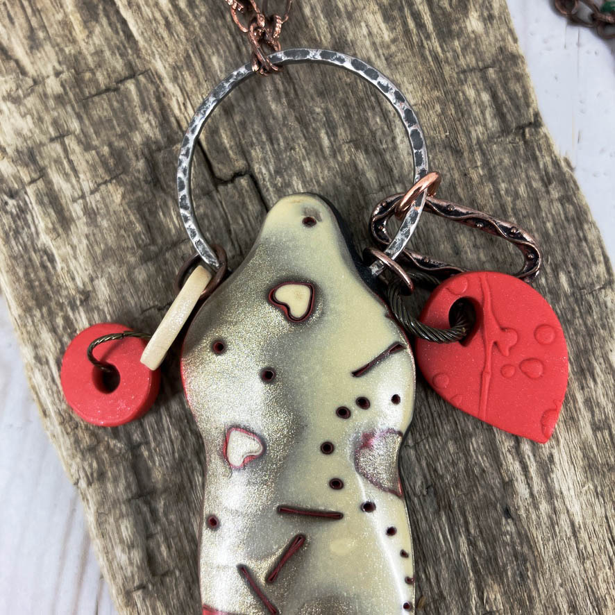 Close up of Symbol of Love Pendant with ring and red polymer clay charms dangling on top. One of a kind necklace by Linda Stiles Smith. 